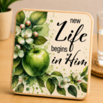 Inspirational wooden coaster featuring the phrase "New Life Begins in Him" with a vibrant green apple surrounded by delicate apple blossoms, flower buds, and lush green leaves. Faith-based Christian coaster with elegant watercolor botanical artwork and natural wood finish, perfect for home décor, religious gifts, Bible study groups, Easter celebrations, and everyday encouragement.